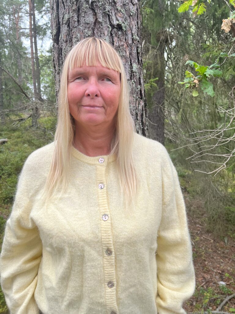 Bild på Carina, stående framför en trädstam i skogen